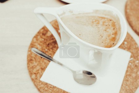Téléchargez les photos : Tasse à café sur plaque de liège, vintage filtrée. Concept Latte. Café au lait dans une tasse blanche. Papier peint café. Table de petit déjeuner. Boissons du matin. Cappuccino en tasse blanche. Americano avec du lait sur la table. - en image libre de droit