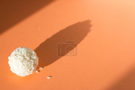 Cremige Bonbons auf pfirsichfarbenem Hintergrund. Kokosraffaello auf Pfirsichfarbenbanner. Raffaello Ball im Sonnenlicht. Simplizitätskonzept. Süßes Dessert isoliert. Pralinenbonbons im Sonnenschein mit Schatten.