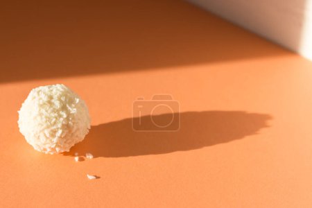Cremige Bonbons auf pfirsichfarbenem Hintergrund. Kokosraffaello auf Pfirsichfarbenbanner. Raffaello Ball im Sonnenlicht. Simplizitätskonzept. Süßes Dessert isoliert. Pralinenbonbons im Sonnenschein mit Schatten.