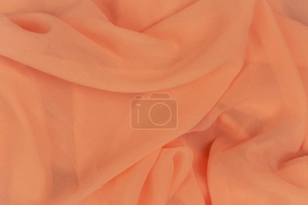 Pfirsichfarbener Hintergrund. Aprikosenmuster. Chiffonstoff. Falten Sie Satin Hintergrund. Seidenstoff Hintergrund. Orange Textilien. Elegante Dekoration. Textur der Kleidung mit Kopierraum. 