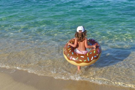 Photo for Little girl with an inflatable ring goes swimming in the sea, back view - Royalty Free Image