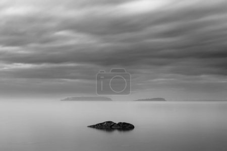 Vista de larga exposición de una roca en el lago Trasimeno Umbría, con islas en el fondo y cielo malhumorado.