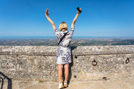 Foto de Young beautiful woman visits the sights of the Republic of San Marino, Italy. She stay in Second tower - Cesta and admiring the view of panorama of San Marino - Imagen libre de derechos