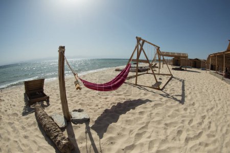 A burgundy hammock is installed on the sandy shore of the Red Sea
