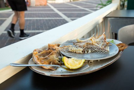 sur la table, sur l'assiette il y a des os du poisson mangé, le repas est terminé