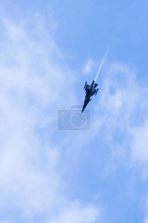 Téléchargez les photos : Avion de chasse supersonique militaire effectue une manœuvre en diagonale du coin supérieur droit au coin inférieur gauche sur fond de ciel bleu - en image libre de droit