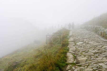 Photo for Silhouettes of a group of adventure seekers in thick fog on a rocky hiking trail in the mountains - Royalty Free Image