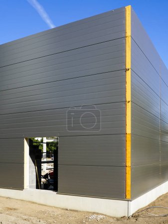 Fachada de paneles sándwich gris de una nueva construcción metálica moderna con aislamiento térmico edificio industrial inacabado