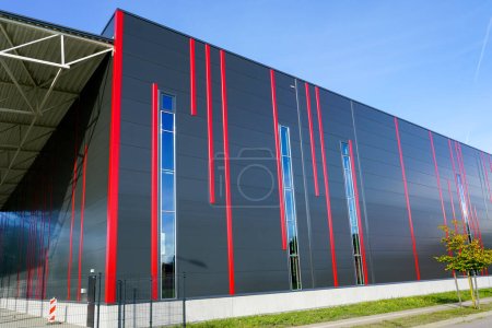 Foto de Fachada de paneles sándwich coloridos de diseño moderno con rayas verticales rojas de un nuevo edificio industrial con aislamiento térmico de construcción metálica - Imagen libre de derechos