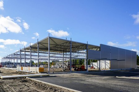 Unfinished steel framework with partially assembled sandwich panel wall and corrugated metal roof panels covering, incomplete new warehouse building