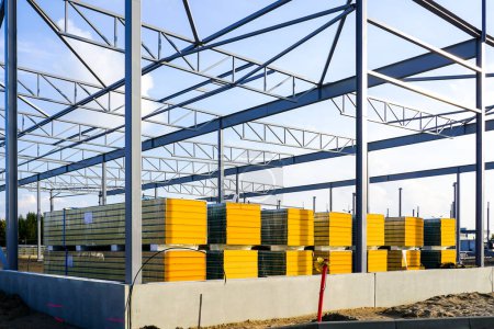 Photo for Assembled steel frame and stacks of sandwich panels for the facade of a new modern industrial building - Royalty Free Image