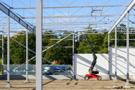 Photo for New building steel framework assembly using self propelled lift platform, unfinished warehouse building - Royalty Free Image