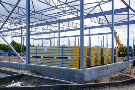 Photo for Steel structure framework building and stacks of sandwich panels for the facade covering of a new modern warehouse - Royalty Free Image