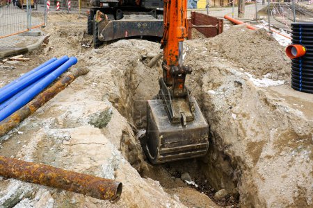 Ein Hydraulikbagger mit Schaufel gräbt in einer Stadtstraße einen Graben für den Austausch unterirdischer Kommunikationsrohre
