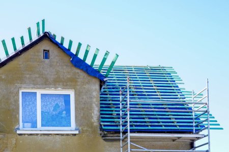 Téléchargez les photos : Nouveau film de toiture et planches imprégnées de planches de bois avant de remplacer le revêtement de toit d'une maison d'habitation, fond bleu ciel - en image libre de droit