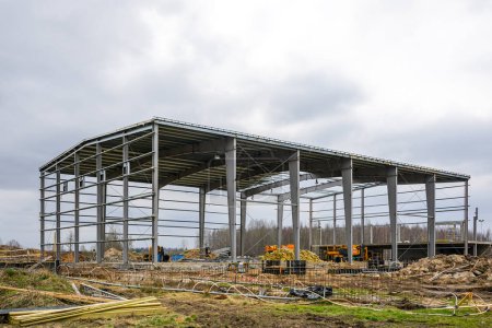 Baustelle mit Metallgerüst eines neuen unfertigen Industriegebäudes, Baumaschinen, Ausrüstung und verschiedenen Materialien