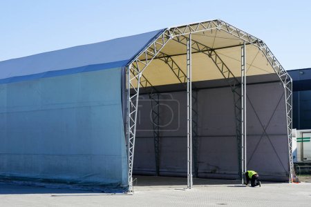 Téléchargez les photos : Hangar de tente à ossature métallique préfabriquée non fini recouvert d'un tissu gris de chlorure de polyvinyle - en image libre de droit