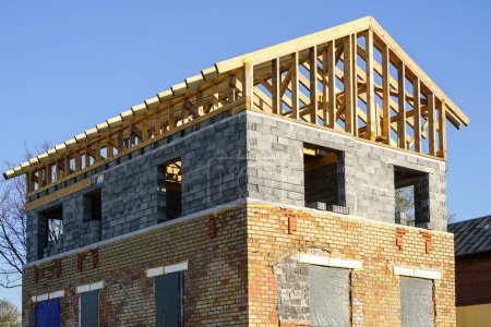 Unfinished residential house with brick and block walls and a wooden beam roof structure, blue sky background