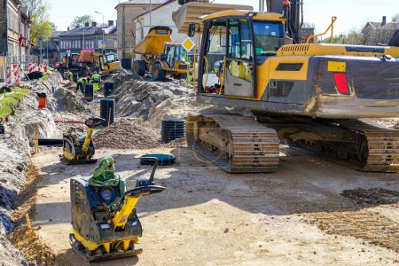 Street reconstruction site view with workers, several excavators, vibratory plate compactors and other machinery