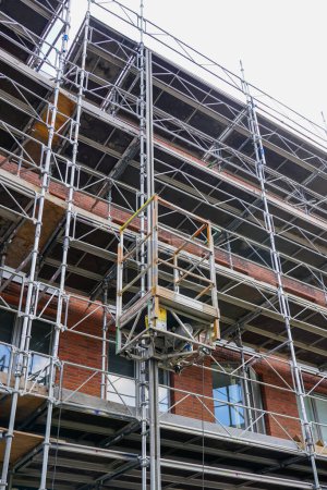 Photo for Repair of the facade of a historic tall house using scaffolding with temporary elevator platform - Royalty Free Image