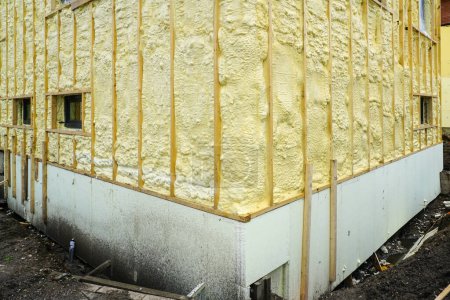 Foto de La fachada de la casa residencial rociada con una capa de espuma de aislamiento térmico de poliuretano antes del revestimiento, aislamiento de cimentación con placas de espuma - Imagen libre de derechos