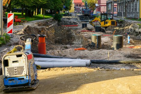 Street reconstruction view, replaced underground pipes, vertical plastic wells, dewatering system, excavators, deep and wide trench, plate compactor