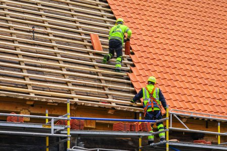 Photo for Two roofers in protective workwear installing new clay tiles, new clay tiles layer covering, new clay tile roofing - Royalty Free Image