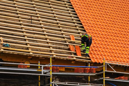 Photo for Roofer in protective workwear installing new clay tiles, new clay tiles layer covering, new clay tile roofing - Royalty Free Image