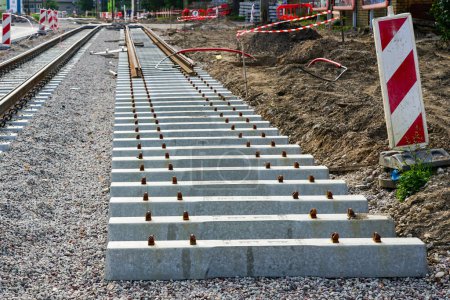 Téléchargez les photos : Nouveau site de construction de voies de tramway avec traverses en béton sur la base des décombres, panneaux d'avertissement et barrières d'avertissement en plastique - en image libre de droit