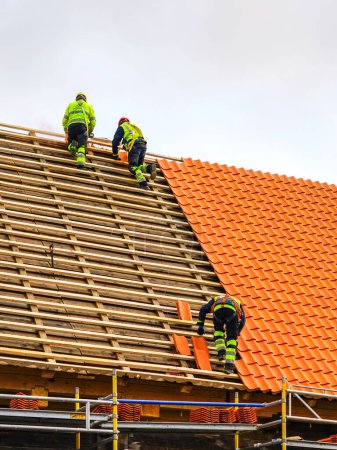 Photo for Three workers in protective workwear installing new clay tiles roof, new clay tiles layer covering, new clay tile roofing - Royalty Free Image