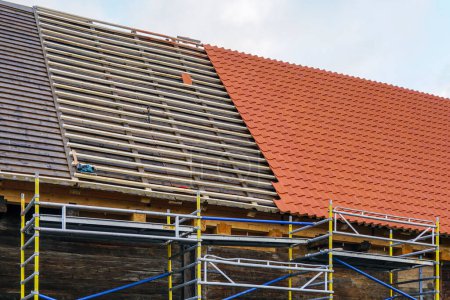 Photo for Installation of new red clay tiles on new wooden battens on the roof of a historic house, new covering of a tiled roof - Royalty Free Image