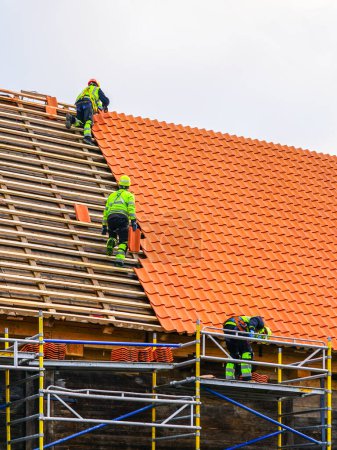 Photo for Three roofers in protective workwear installing new clay tiles, new clay tiles layer covering, installing clay roof tiles - Royalty Free Image