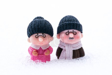 Miniature figures of two old retired people, a woman and a man, in deep snow, life difficulties and togetherness concept, white snow background