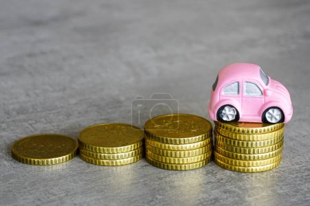 Ein rosafarbenes Miniaturauto auf einem Stapel von Münzen zunehmender Höhe, wachsender Stapel von Münzen, das Konzept der Erhöhung der Betriebskosten des Autos
