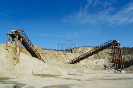 Huge rusty metal structures for transporting rocks in a dolomite mining quarry, gravel crushing, sorting, conveying, blue sky background