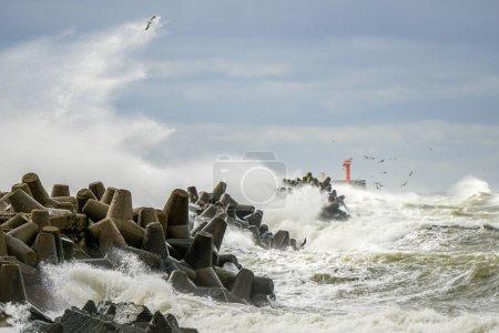 Tempête en mer, fortes vagues s'écrasant contre les brise-lames en béton du port, fortes éclaboussures blanches, mouettes volant, tempête ouragan, puissance de la nature