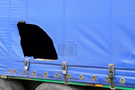 Remolque de camión con toldo azul dañado, problema de robo de carga cortando el toldo, robos de mercancías de remolques de carga, robo de mercancías, corte de toldo