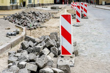 Street paving with historical hammered cubes shape granite paving stones, , cubes rocks, cubes stones, red and white striped vertical warning sign