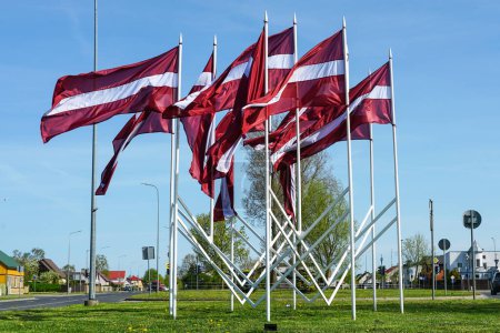 Many national flags of Latvia fluttering in the wind as a decoration of the city during national holidays, blue sky background