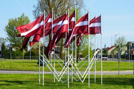 Many national flags of Latvia fluttering in the wind as a decoration of the city during national holidays, blue sky background
