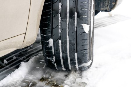 Téléchargez les photos : Pneu de voiture de marche d'été dans la neige, conduite avec des pneus impropres à la saison, circulation dangereuse et dangereuse, pneu de marche d'été sur la route glissante de neige - en image libre de droit