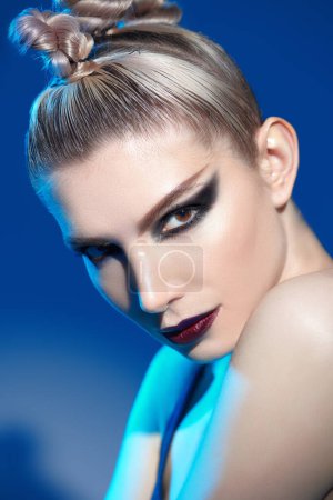 Maquillage et cosmétiques. Photo d'un beau modèle féminin au maquillage sombre et agressif. Portrait studio sur fond bleu. 