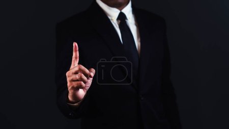 Geschäftsmann zeigt Zeigefinger vor dunklem Hintergrund.