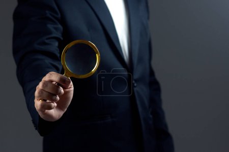 Businessman is using magnifying glass against dark background.