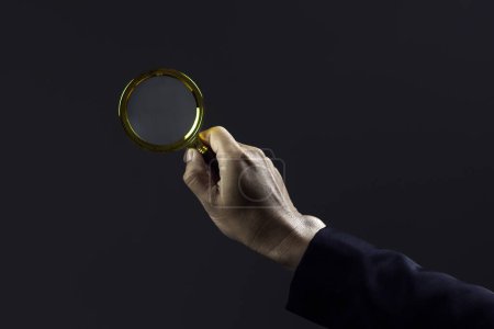 Close-up hand of businessman use magnifying glass against dark background.