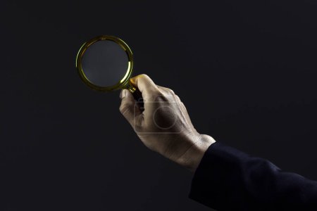 Close-up hand of businessman use magnifying glass against dark background.