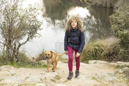 Foto de Cabello rizado y rubio, mujer montañera y su perro paseando por las montañas. - Imagen libre de derechos