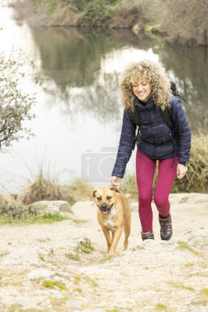 Photo for Curly and blonde hair, mountaineer woman and her dog walking through the mountains. - Royalty Free Image