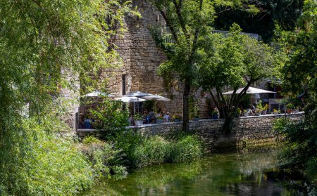 Téléchargez les photos : Arbois, France - July 17, 2020: restaurant and terrace at the river Cuisance in the centre of Arbois with old wall a summers day in the Jura, France. - en image libre de droit