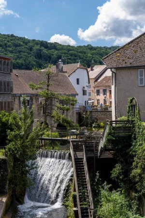 Téléchargez les photos : Arbois, France - July 17, 2020: Waterfall in the centre of Arbois with old houses and stairs on a summers day in the Jura, France. - en image libre de droit